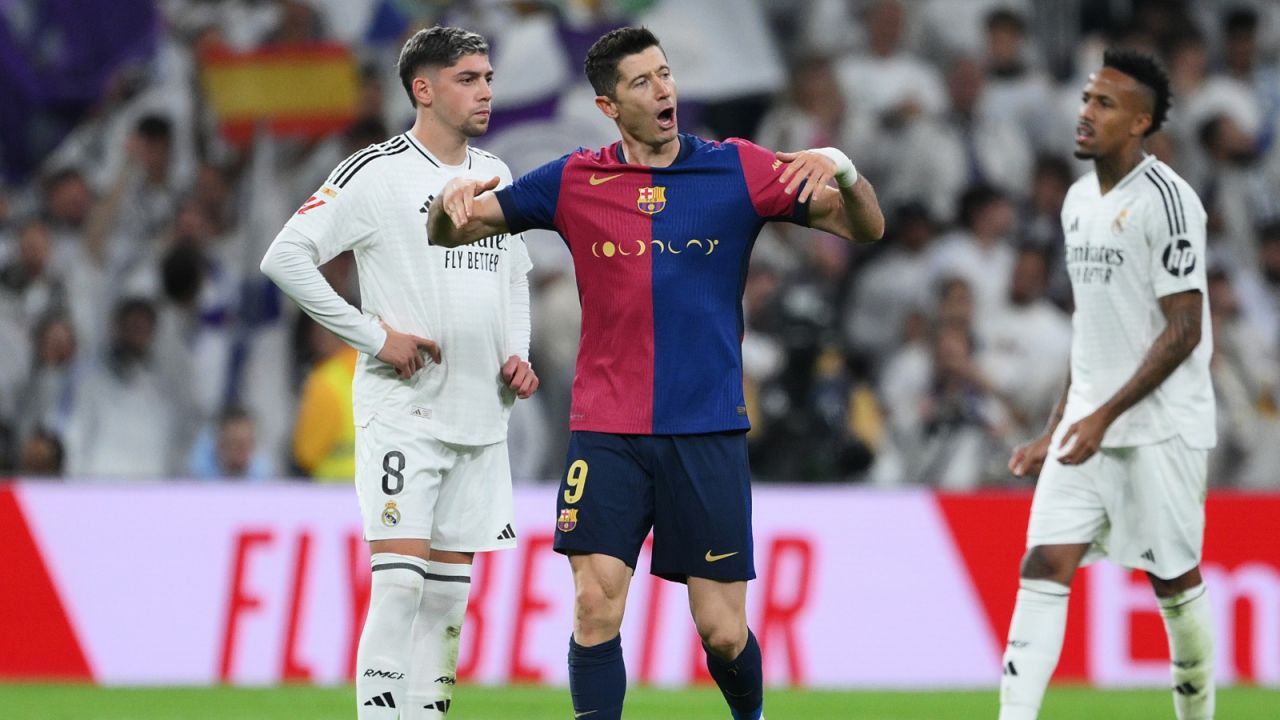 Zdjęcie przedstawia piłkarzy FC Barcelony i Realu Madryt w akcji podczas meczu El Clásico. Na pierwszym planie widać zawodnika Barcelony walczącego o piłkę z rywalem w białym stroju Realu. Tłum na trybunach i intensywna rywalizacja oddają emocje jednego z najbardziej prestiżowych spotkań sezonu La Liga 2024/25.