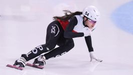 Kornelia Woźniak (fot. Getty Images) Zawodniczka w stroju reprezentacji Polski podczas wyścigu short track na lodowisku, w pozycji dynamicznej przy zakręcie, z widocznymi łyżwami do jazdy szybkiej i kaskiem z numerem 54