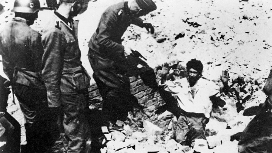 Kwiecień – maj 1943, powstanie w getcie warszawskim. Niemieccy żołnierze trzymają na muszce mężczyznę, powstańca wychodzącego z podniesionymi rękami z kryjówki ¬ – bunkra czy piwnicy. Fot. ŻIH / Forum