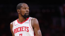 Kevin Durant (fot. Getty Images) Na zdjęciu widać Kevina Duranta ubranego w biały strój Houston Rockets z czerwonymi akcentami i numerem 7. Zawodnik wygląda na skupionego i spogląda w bok, prawdopodobnie obserwując rozwój akcji na boisku. Pot na jego ramionach i intensywny wyraz twarzy sugerują, że znajduje się w środku zaciętego meczu. Zdjęcie może symbolizować jego nowy etap kariery związany z klubem z Houston