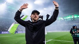 Eugen Polanski (fot. Getty Images) Na tle rozświetlonego stadionu, w atmosferze pełnej emocji i oczekiwania, Eugen Polański stoi na murawie z uniesionymi ramionami, jakby w geście powitania lub triumfu. Ubrany w czarną kurtkę i czapkę, zwraca się ku tłumowi kibiców, którzy zapełnili trybuny, tworząc żywiołową scenerię. W tle powiewa ogromna flaga w barwach zieleni, bieli i czerni — symboliczny akcent Borussii Moenchengladbach — a obok niego widoczna jest klubowa maskotka, dodająca scenie nieco lekkości (fot. Getty Images)
